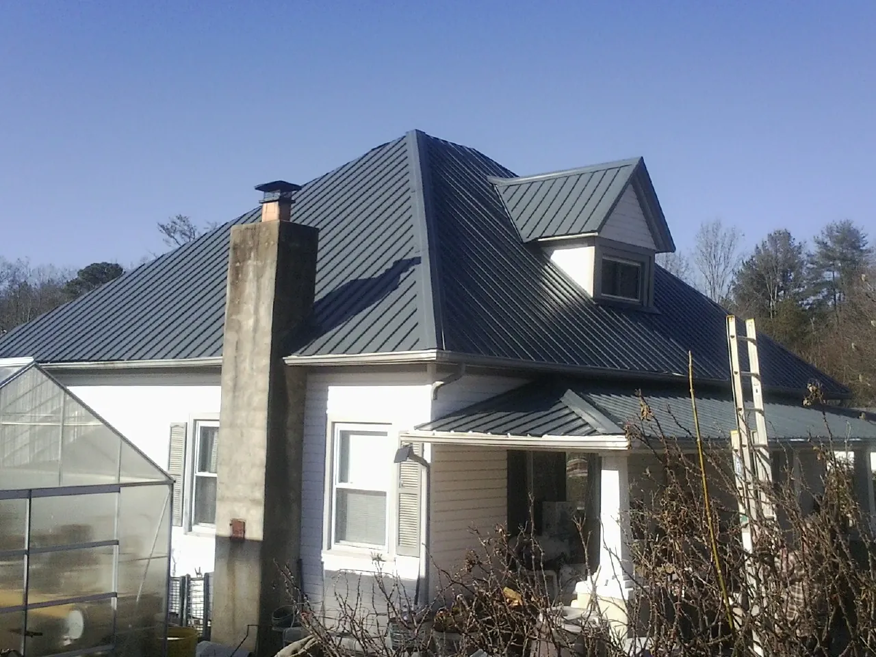 Dark blue standing seam metal roof on a white farmhouse with dormer — Slate & Tile Roof Repair by Roofing Brothers in Silver Creek