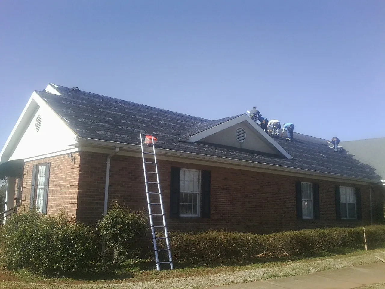 Crew tearing shingles off a brick ranch roof with a ladder set — Emergency Roof Repair work by our crew in Silver Creek