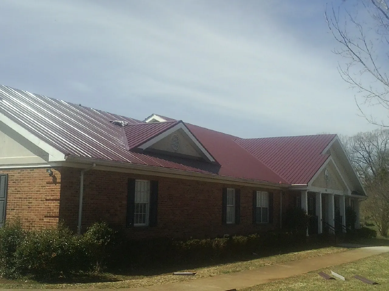 Red metal roof with gabled entries on a long brick building, from a Hail Damage Roof Repair job in Silver Creek