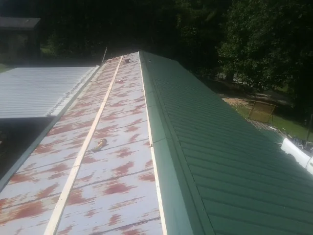 Old rusted panels beside newly installed green metal roofing — Wind Damage Roof Repair by Roofing Brothers in Silver Creek