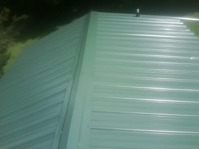 New green metal panels meeting at the ridge of a roof — Flat Roof Repair work by our crew in Silver Creek