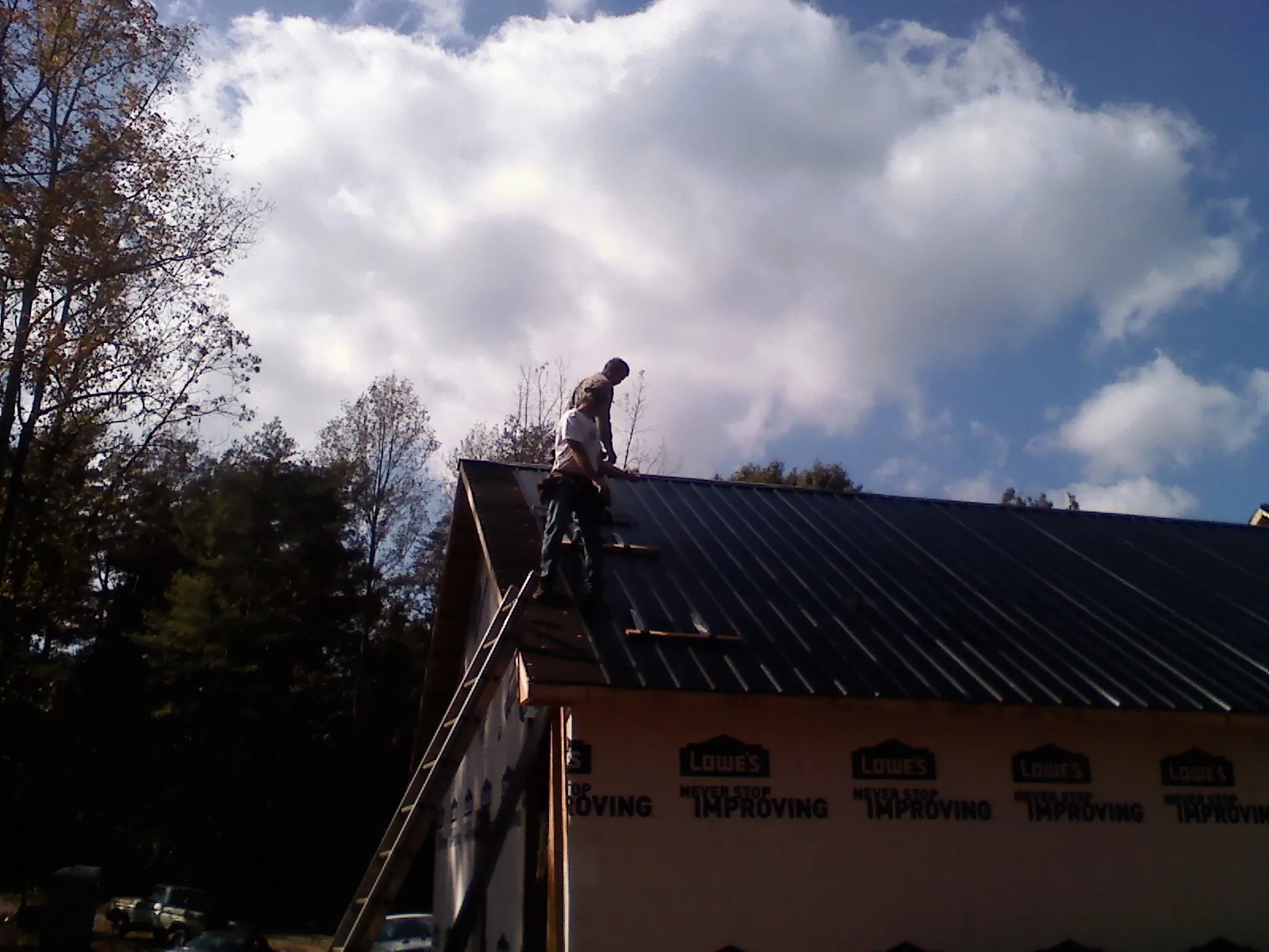 Roofer fastening dark metal panels high against a cloudy sky, from a Roof Inspection job in Silver Creek