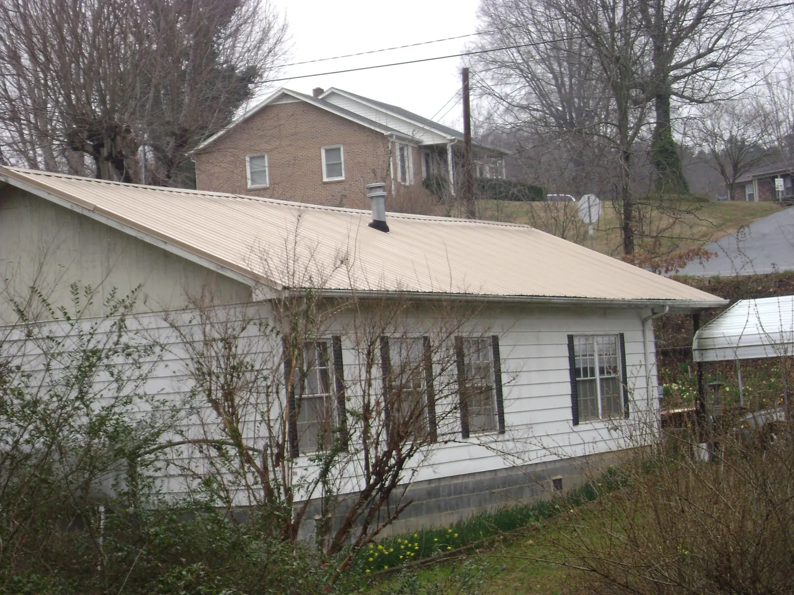 Tan metal roof on a white sided house set into a hillside — Commercial Roofing by Roofing Brothers in Silver Creek